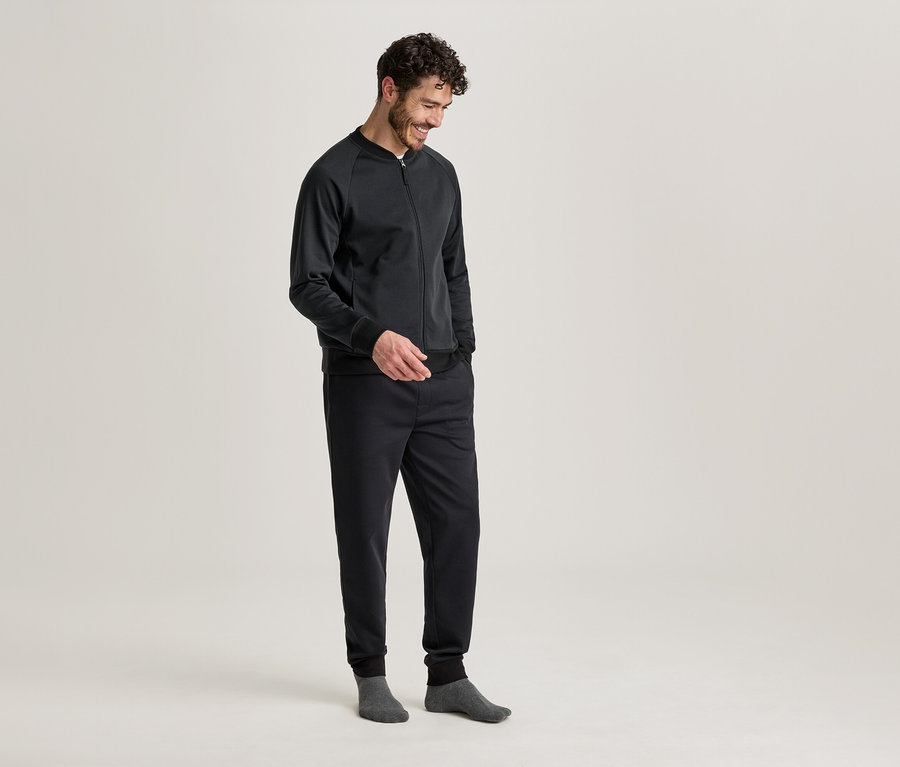 Homme en veste et pantalon sombres, les mains dans les poches, portant des chaussettes grises.