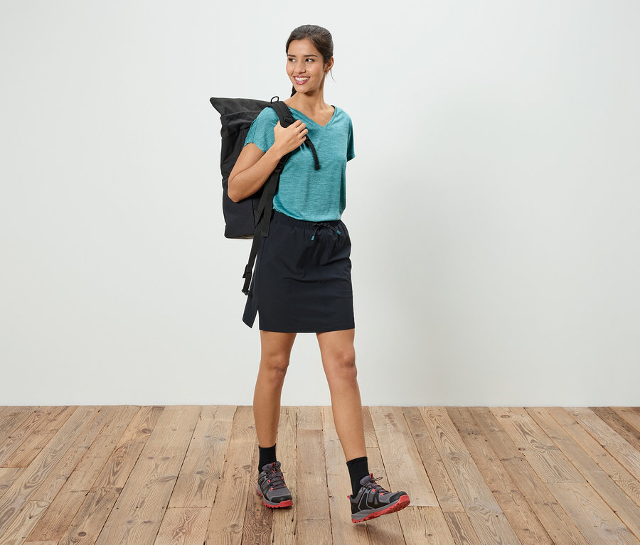 Une femme avec un sac à dos se tient sur un plancher en bois.
