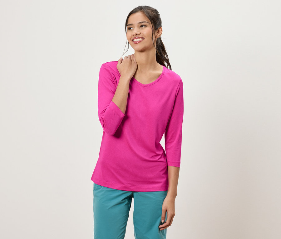 Femme avec queue de cheval portant un haut rose à manches trois-quarts et un pantalon turquoise.