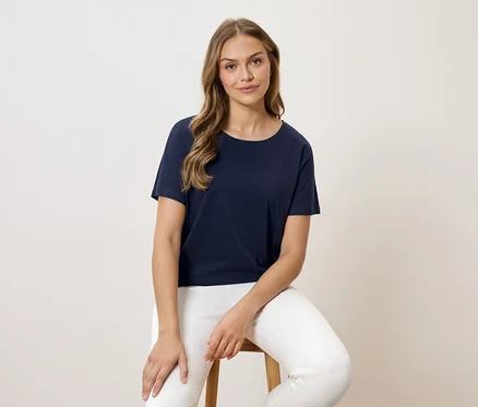 Femme assise sur un tabouret, portant un t-shirt bleu marine et un pantalon blanc.