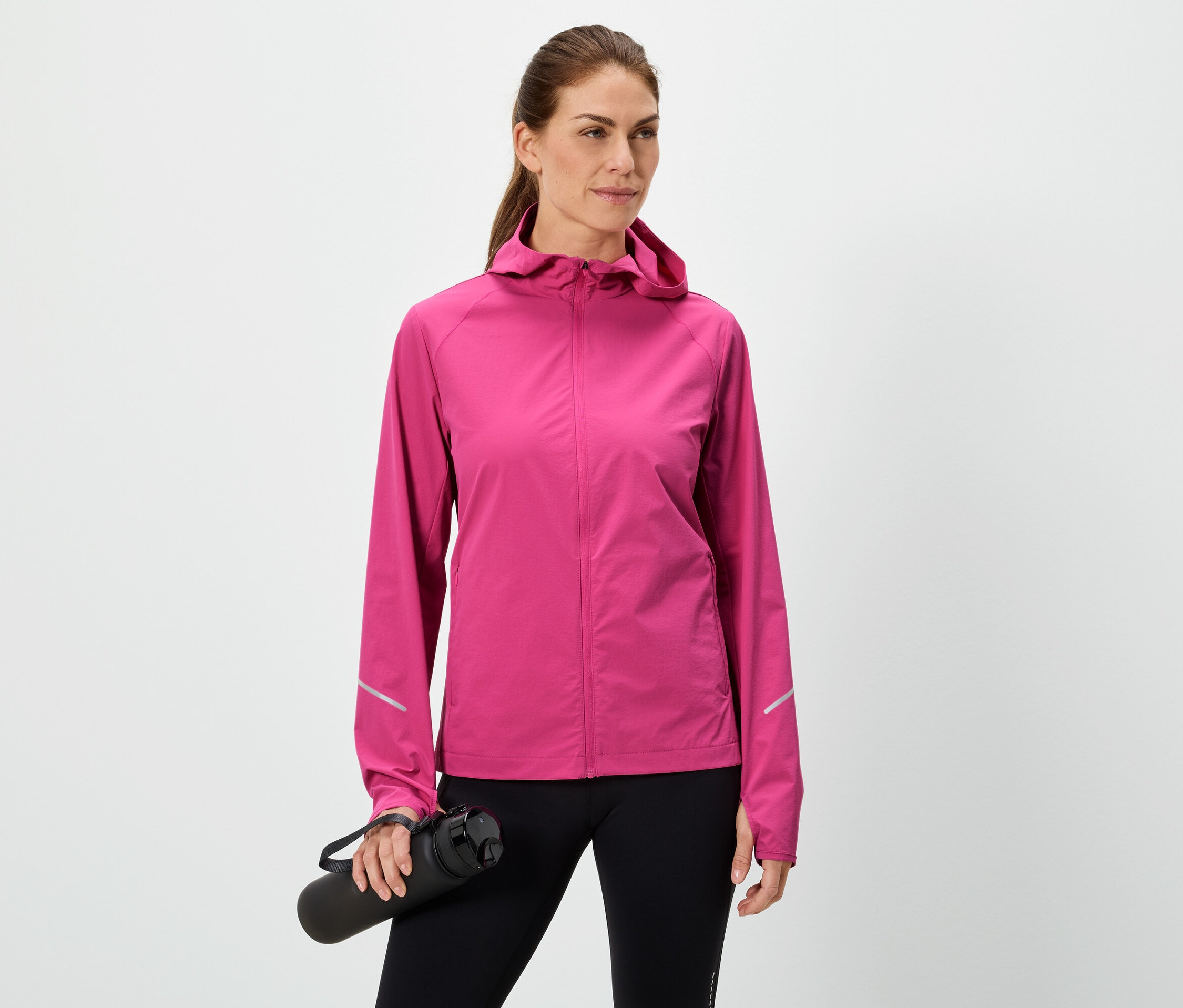 Femme tenant une bouteille d'eau noire, portant une veste rose et un legging noir sur fond blanc.