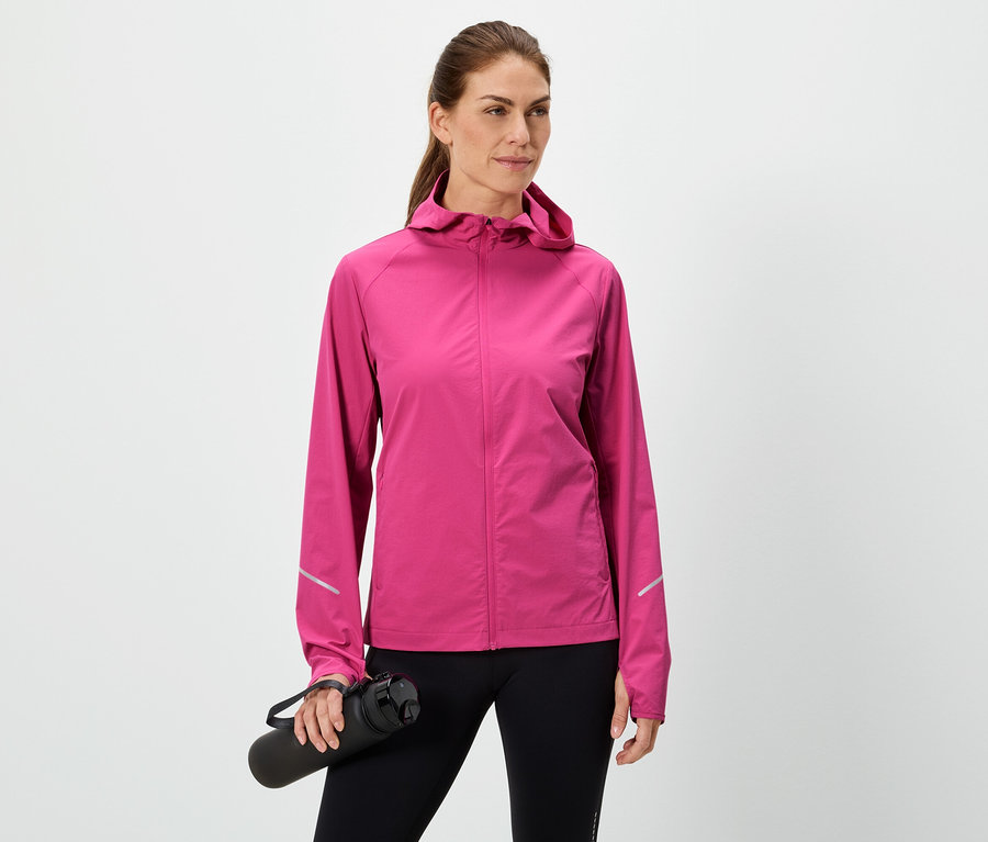 Femme tenant une bouteille d'eau noire, portant une veste rose et un legging noir sur fond blanc.