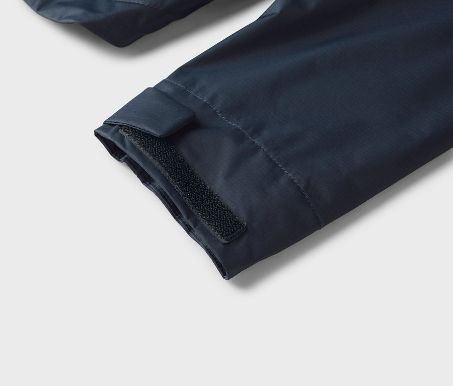 Gros plan sur la manche bleu marine d'une veste avec une fermeture velcro au niveau du poignet.