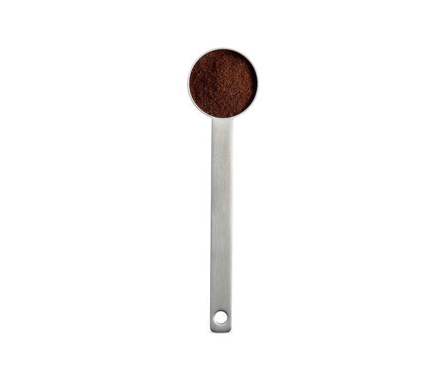 Une cuillère doseuse argentée remplie de café moulu.