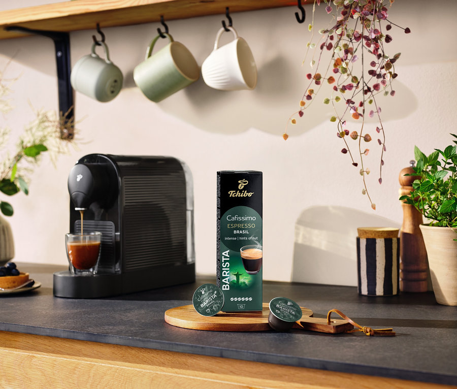 Une machine à café noire prépare du café dans un verre à côté d'un paquet de 10 capsules Espresso Brasil.