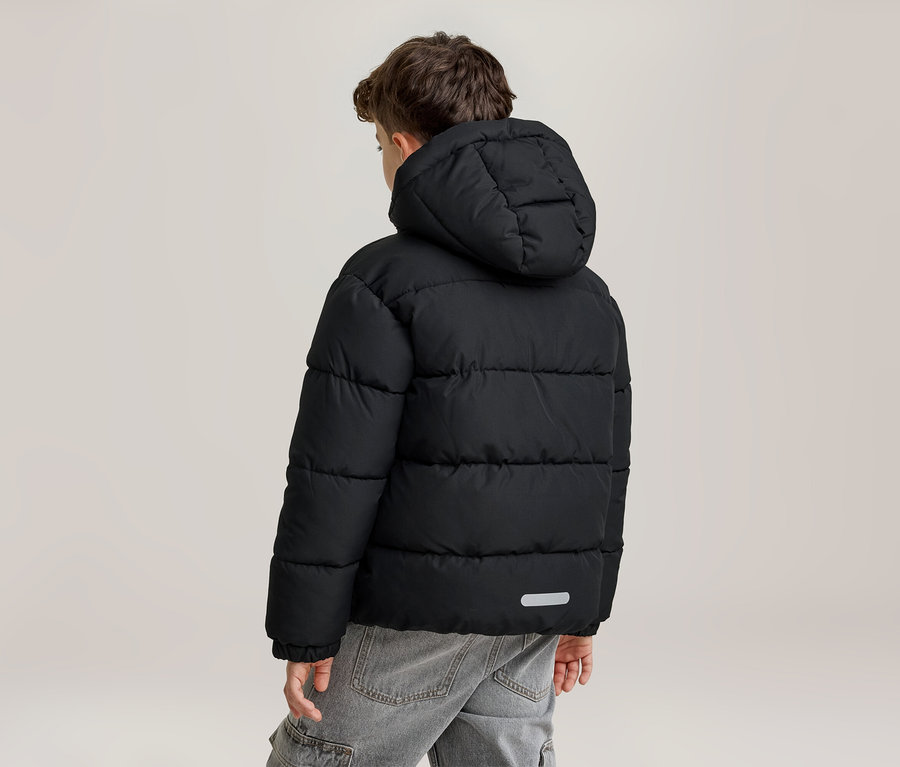 Un jeune garçon vu de dos, portant une doudoune noire à capuche et un jean gris. La veste présente des surpiqûres horizontales et une bande réfléchissante dans le bas du dos.