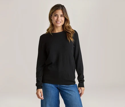 Femme souriante portant un haut noir à manches longues et un jean bleu.