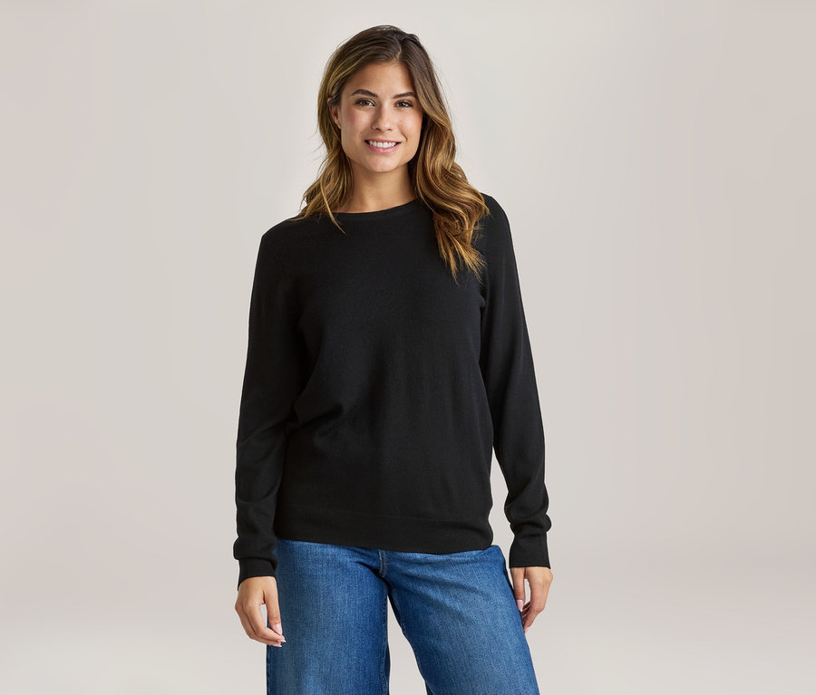 Femme souriante portant un haut noir à manches longues et un jean bleu.