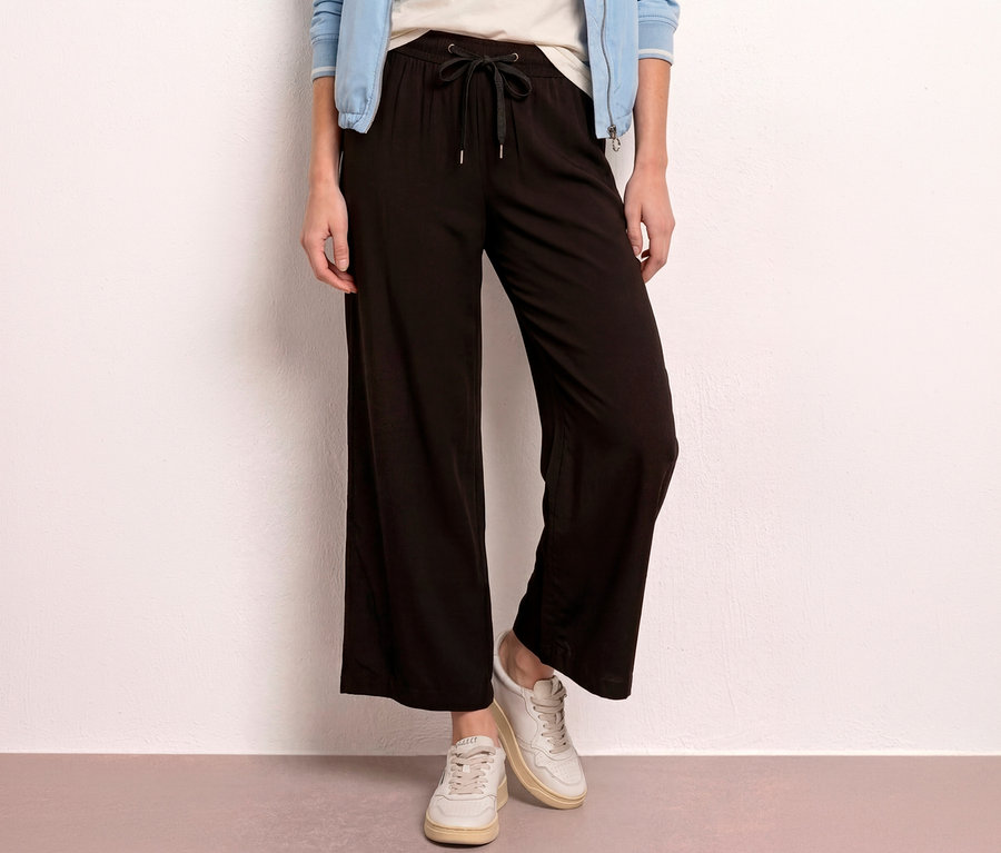 Une personne porte un culotte 7/8 Street One « EMMA » noir avec un cordon de serrage, un t-shirt clair, une veste bleu clair et des baskets claires.