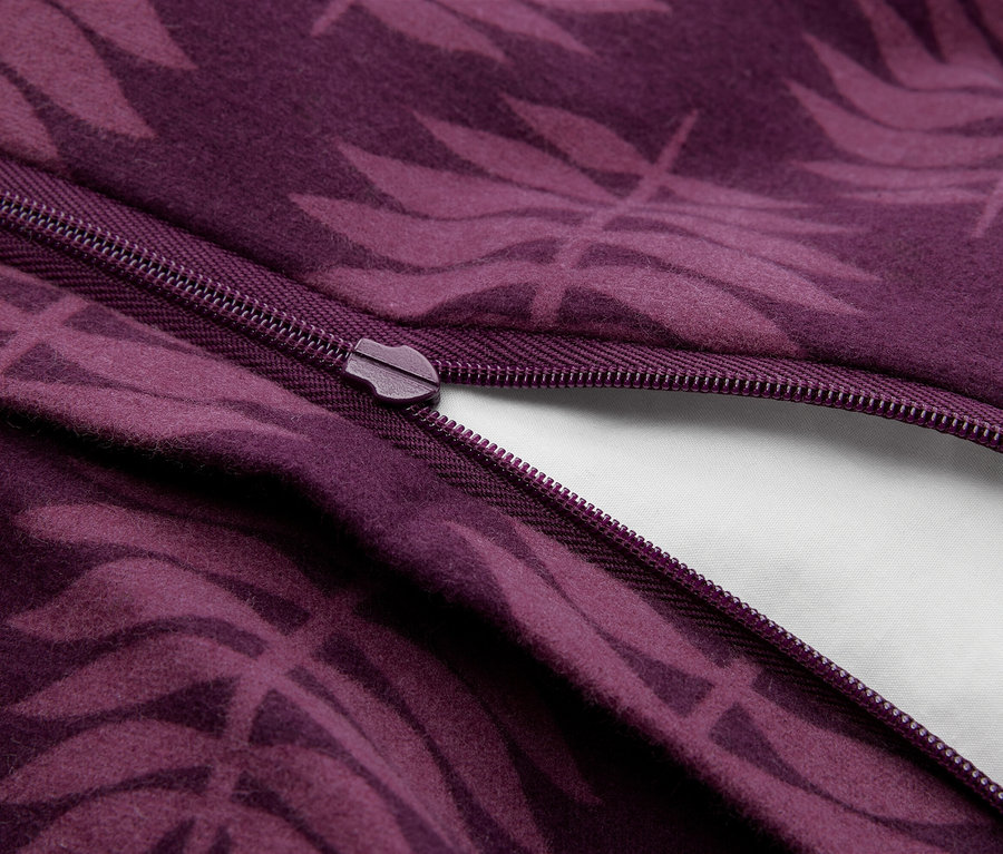 Gros plan d'un tissu violet avec un motif de feuilles plus foncé, partiellement dézippé, révélant un tissu blanc en dessous.
