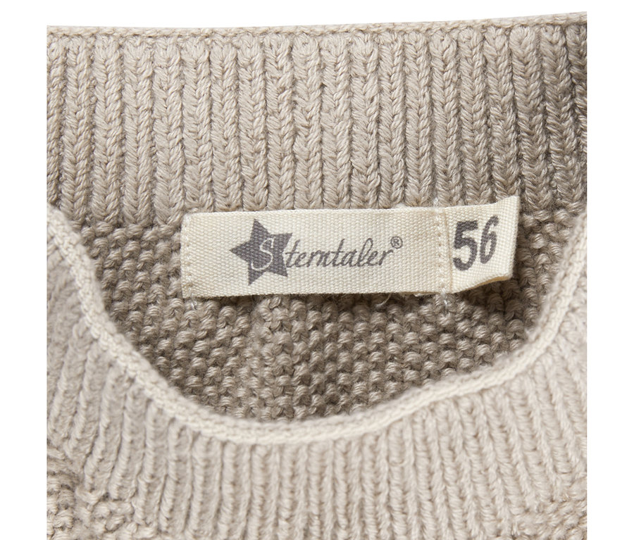 Gros plan d'une étiquette blanche Sterntaler avec la taille 56, cousue sur un pantalon bébé tricoté beige.
