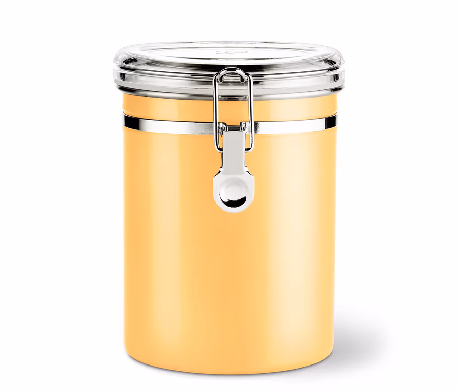 Un récipient de stockage jaune avec une fermeture argentée et un couvercle transparent se trouve sur une surface blanche.