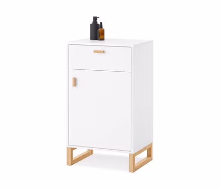 Armoire blanche avec un tiroir et une porte, tous deux avec des poignées en bois, reposant sur des pieds en bois. Sur le dessus, une bouteille pompe noire et une bouteille spray ambrée.