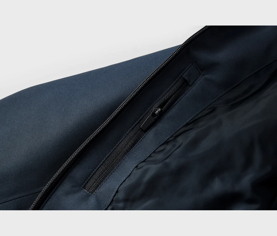 Gros plan d'une veste bleu foncé montrant une fermeture éclair principale et une fermeture éclair de poche partiellement ouverte sur le rabat intérieur, révélant une doublure bleu foncé.