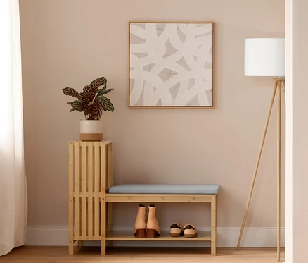 Un hall d'entrée lumineux avec un porte-manteau avec tablette où pendent des vestes. Au centre, un banc avec compartiment à chaussures et étagères en finition lamellé avec un coussin et des chaussures en dessous, à côté d'un lampadaire trépied en bois. À droite, une garde-robe avec banc, aspect lamellé, avec une veste en jean, une écharpe et un sac. À côté, une étagère sur pieds avec 3 compartiments. Deux tapis ronds roses sont posés au sol.