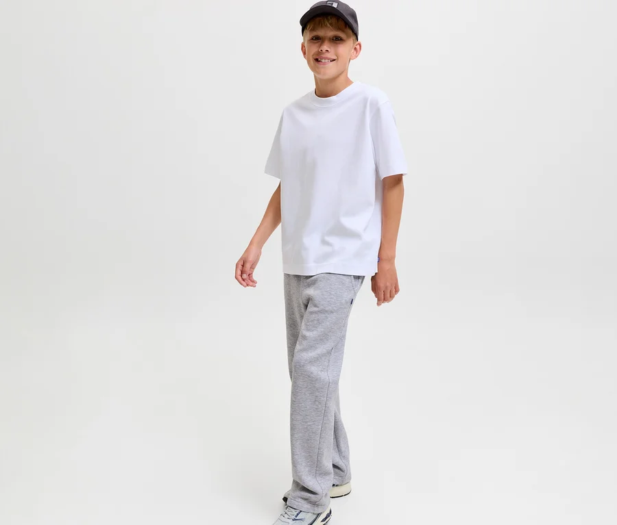 Garçon souriant portant un t-shirt blanc, une casquette de baseball foncée et un pantalon de survêtement gris Jack&Jones Bradley.