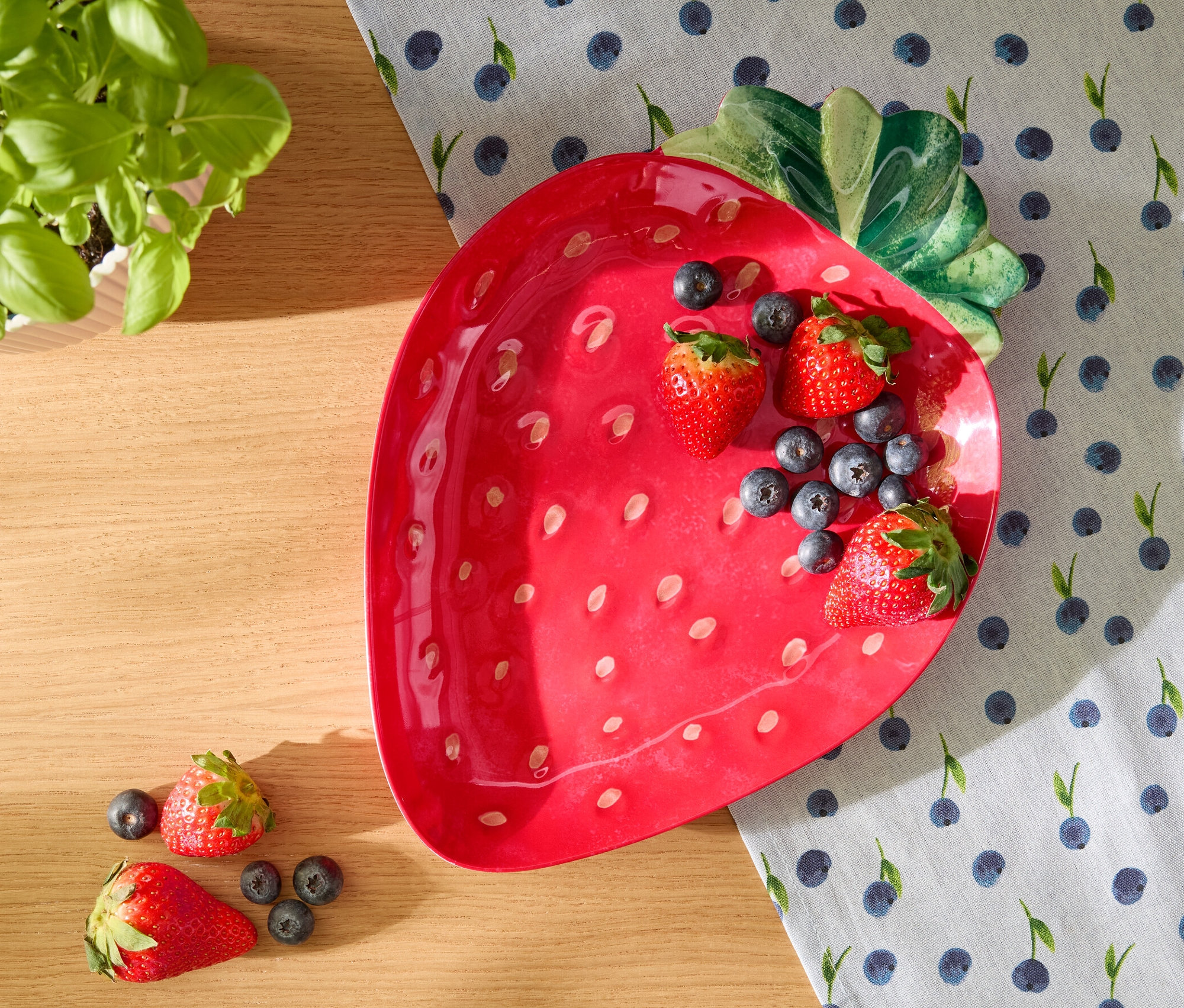 Plat de service rouge en forme de fraise avec des fraises et des myrtilles sur un chemin de table à motif de myrtilles.