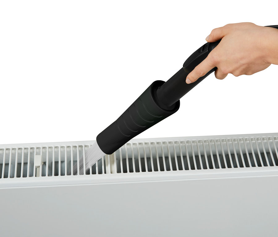 Une main tient un embout d'aspirateur et nettoie un radiateur.