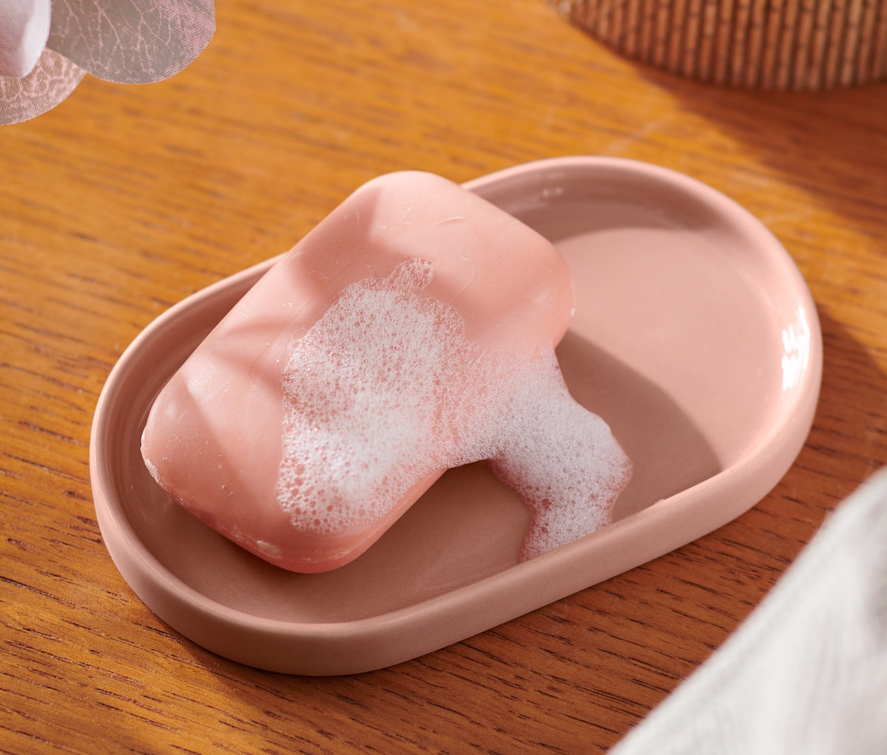 Un porte-savon rose avec du savon est posé sur une table en bois à côté d'une orchidée.