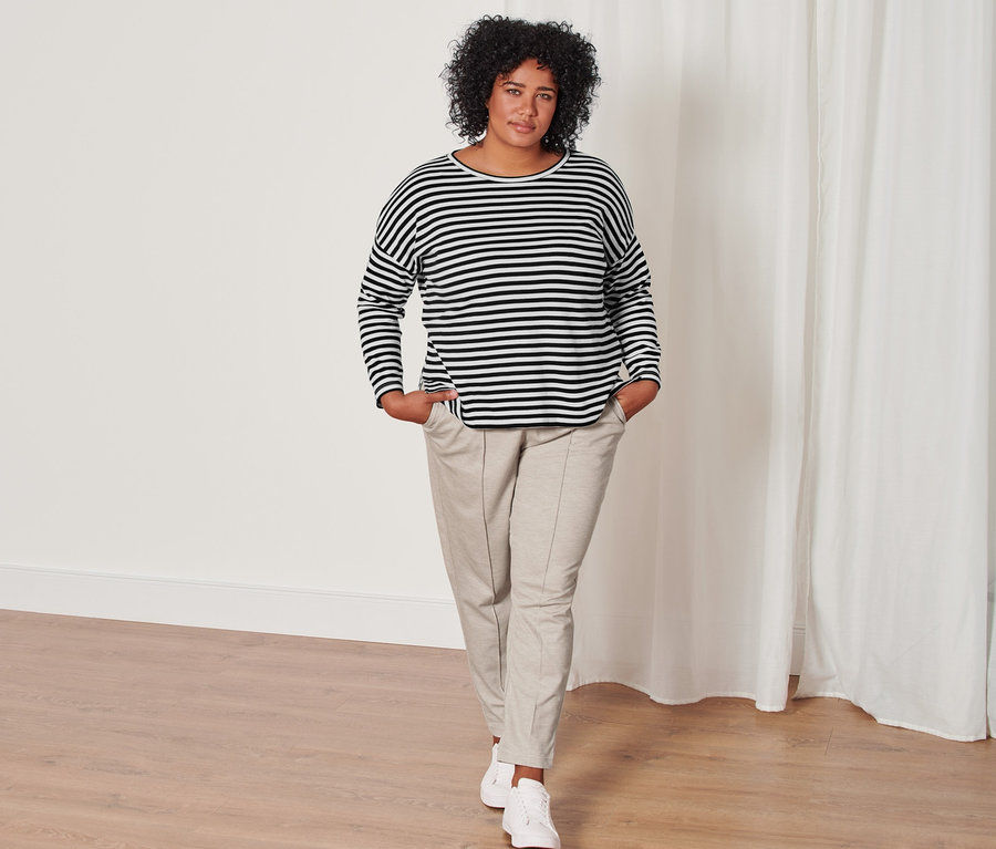 Femme posant en t-shirt manches longues à rayures, noir, et pantalon de jogging avec nervure, beige chiné.