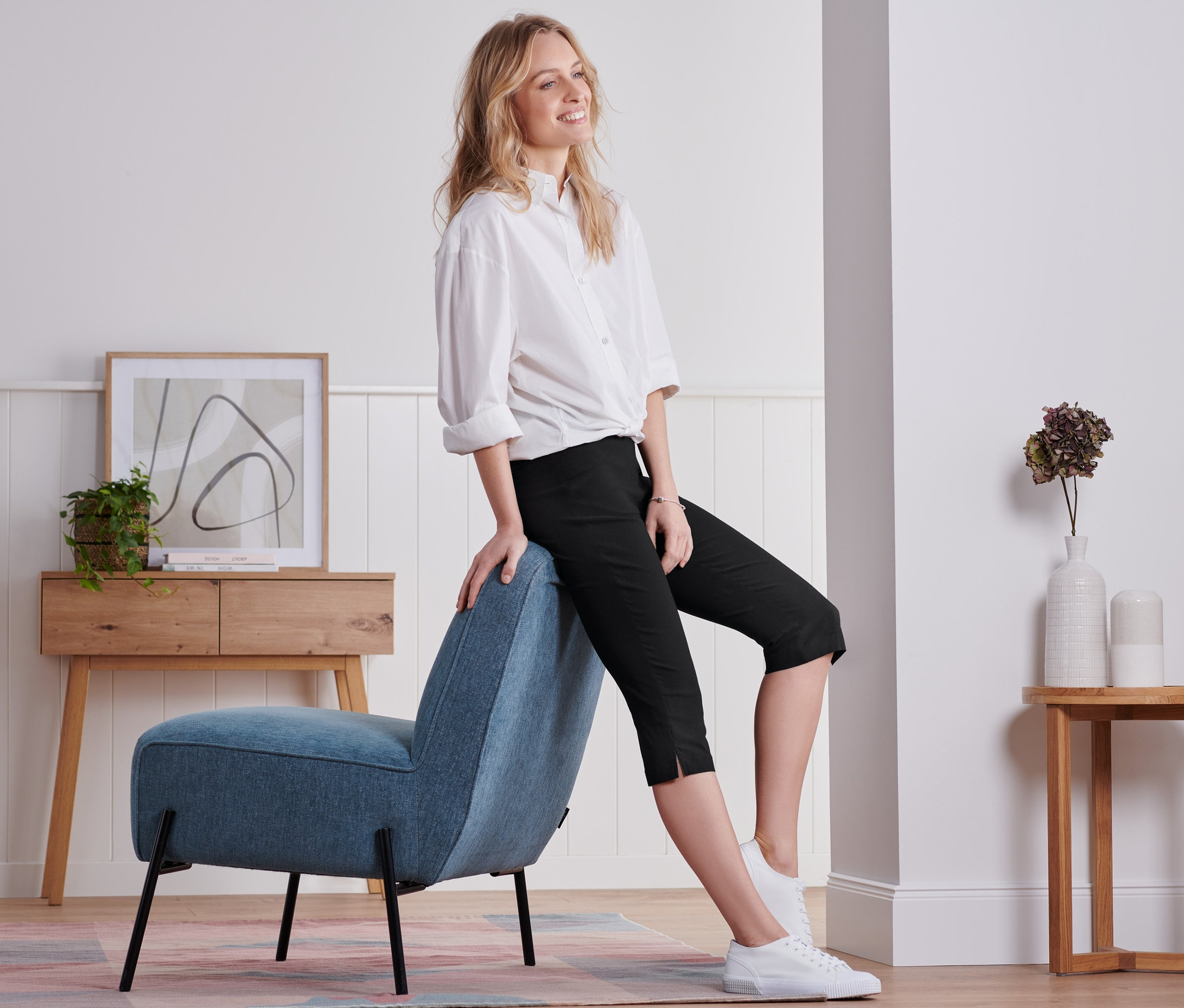 Femme assise sur une chaise bleue portant un pantalon noir 3/4.