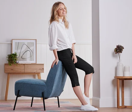 Femme assise sur une chaise bleue portant un pantalon noir 3/4.
