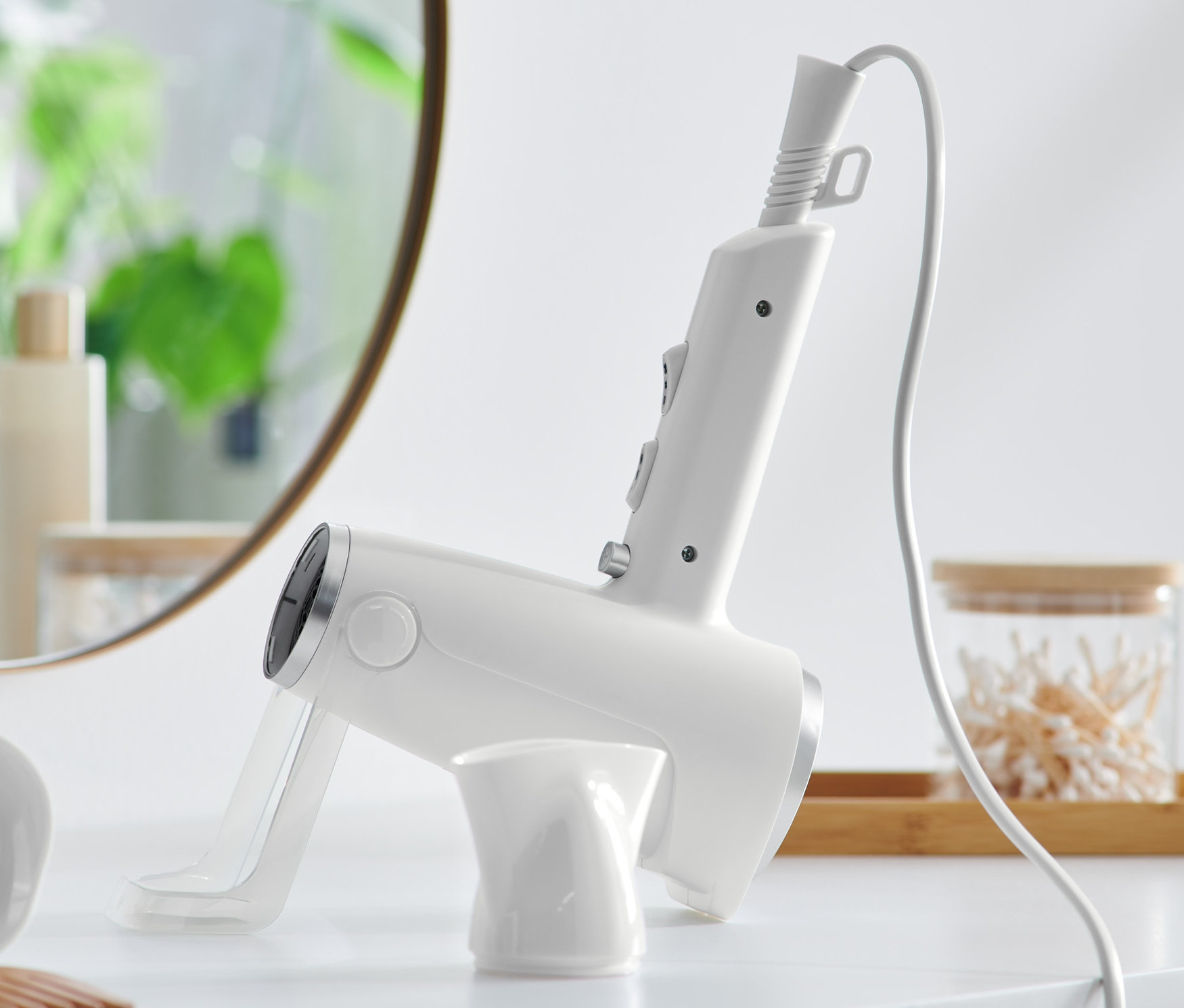Un sèche-cheveux blanc à poser sur une table blanche. Un miroir et des produits cosmétiques en arrière-plan.