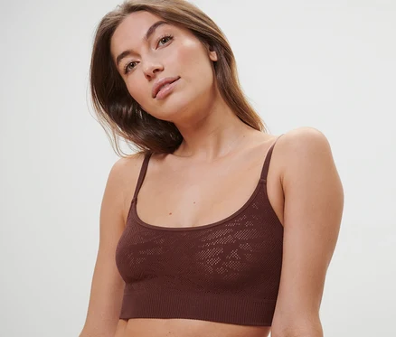 Une femme porte une brassière seamless aspect dentelle marron.