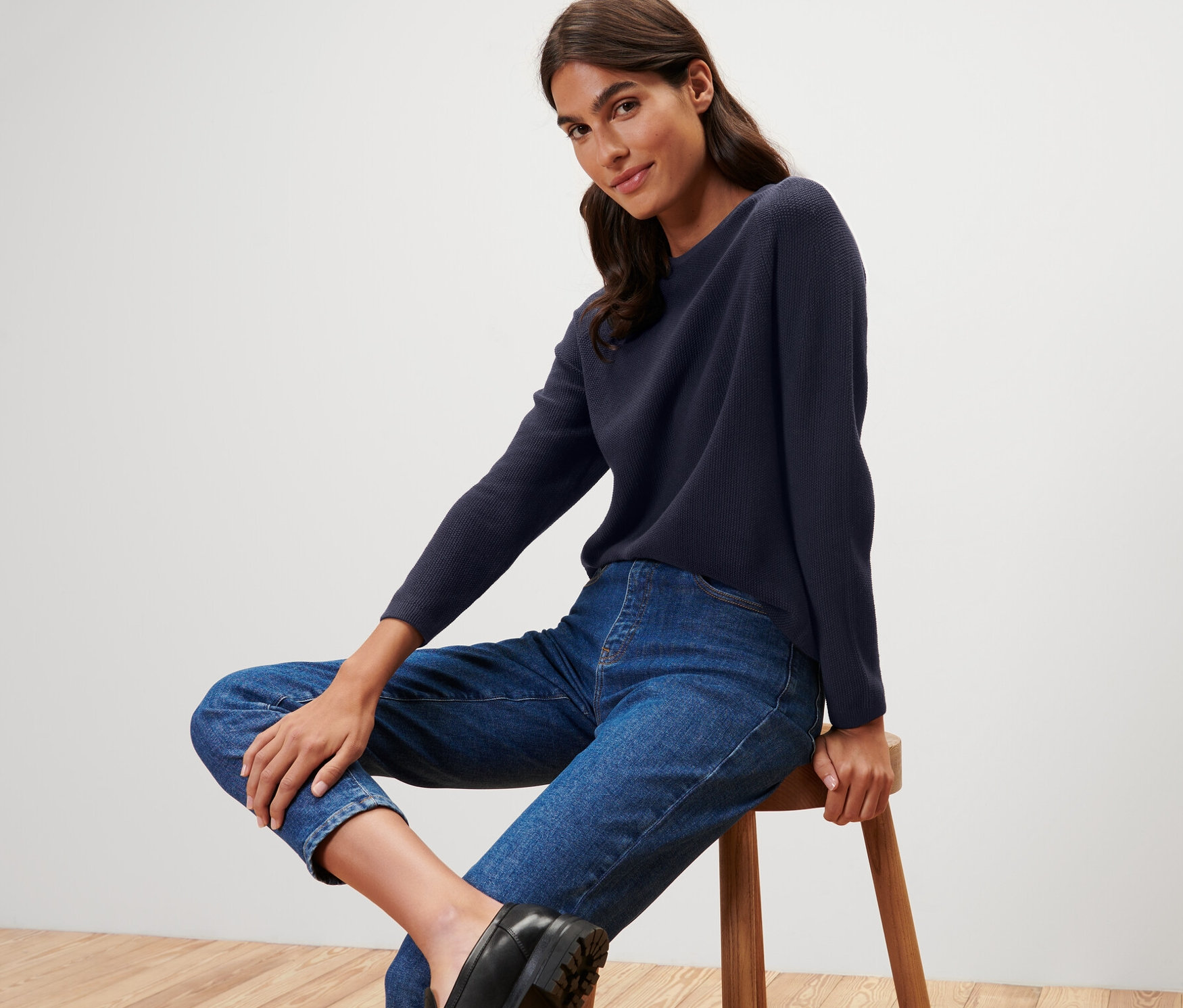 Une femme assise sur un tabouret porte un pull en maille bleu foncé.