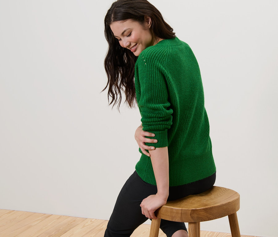 Femme assise sur un tabouret portant un pull en maille vert.