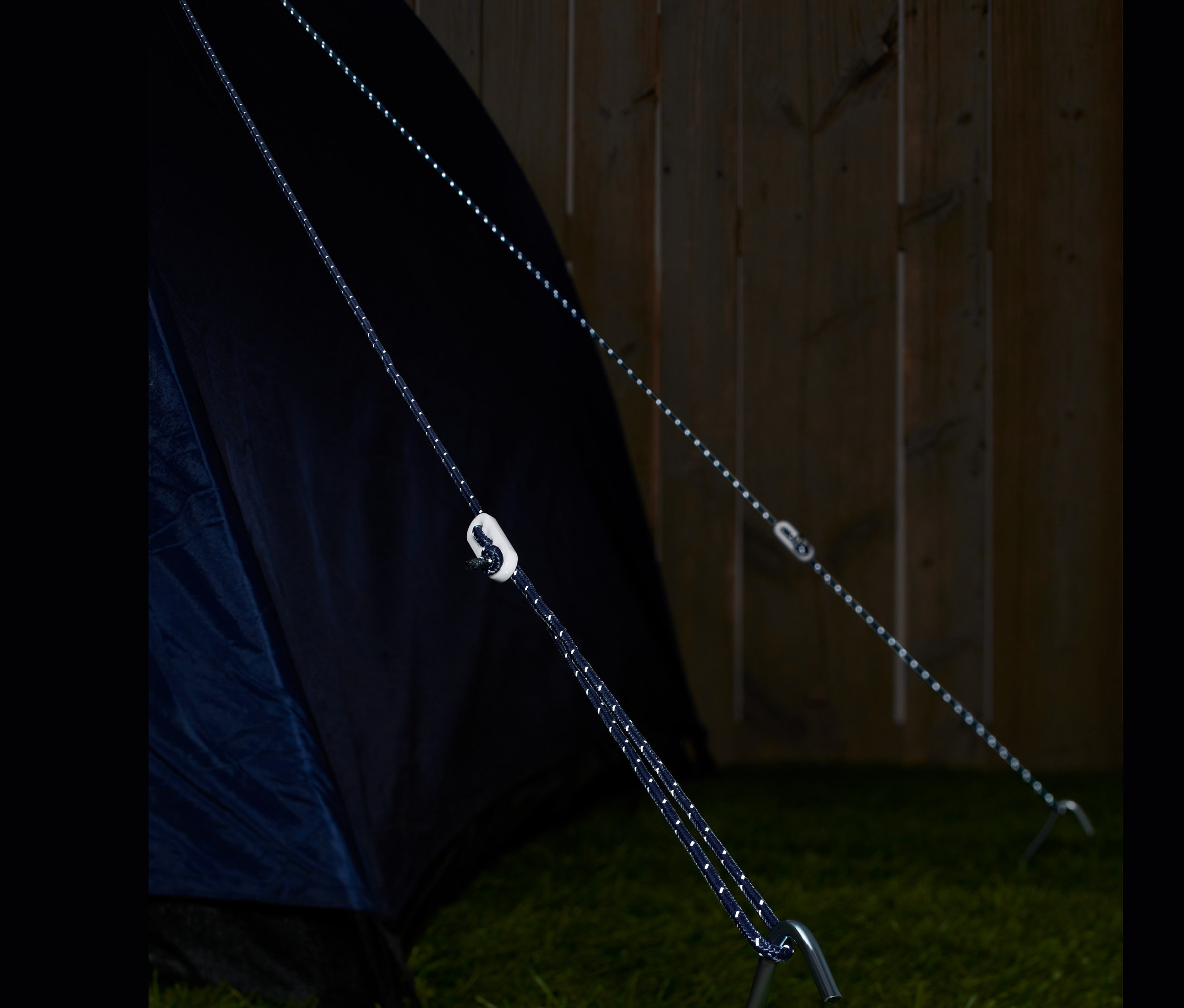 Deux câbles de haubanage réfléchissants sont fixés à une tente et à un piquet dans l'herbe.