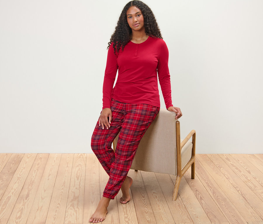 Une femme pose, appuyée contre une chaise, et porte un pyjama en flanelle à carreaux.