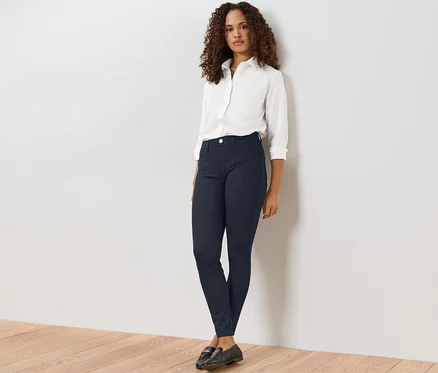 Une femme debout sur un plancher en bois porte une chemise blanche et un jegging foncé.