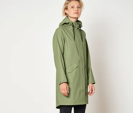 Une femme porte une parka de pluie verte « ciré », un legging noir et des bottes noires.