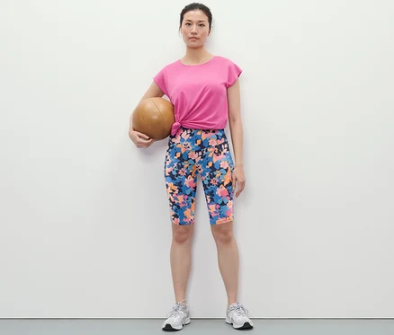 Femme tenant un ballon de médecine et portant un cycliste de sport imprimé intégral, un t-shirt et des baskets.