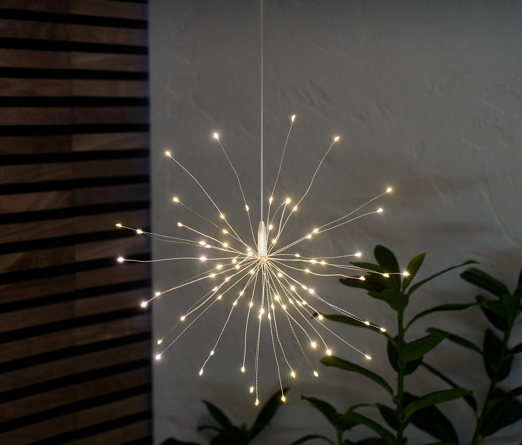 Une branche décorative à LED est suspendue et brille dans la pièce à côté d'une plante.