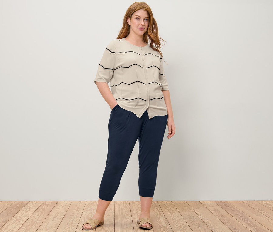 Femme posant en cardigan en maille fine à motif ajouré et pantalon 3/4 en jersey.