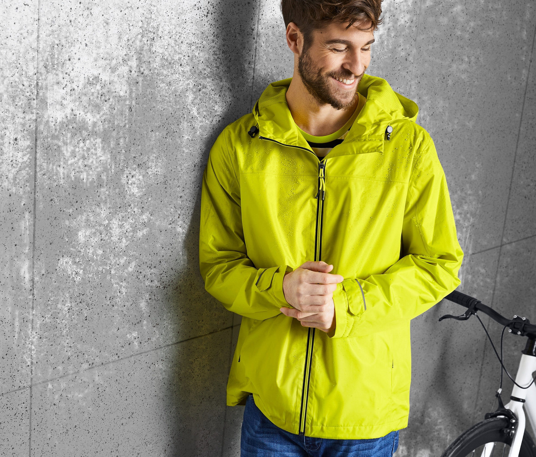Un homme appuyé contre un mur porte une veste de pluie jaune.