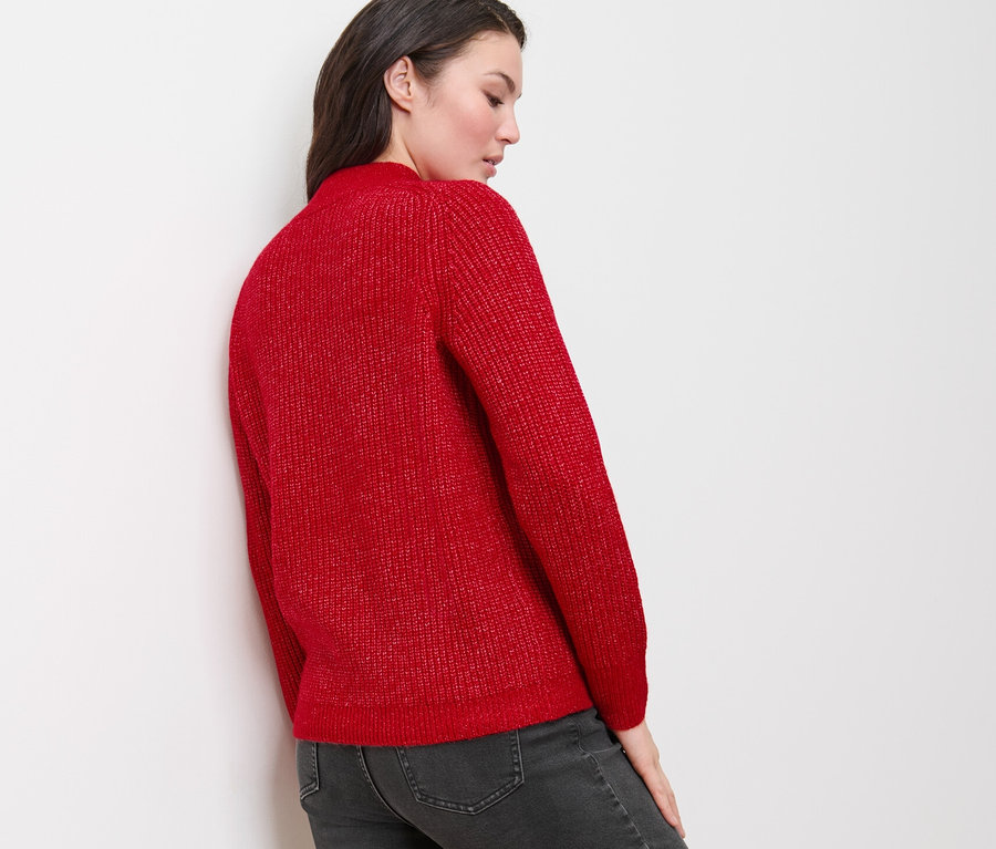 Une femme porte un pull rouge en grosse maille à motif torsadé et un jean gris.