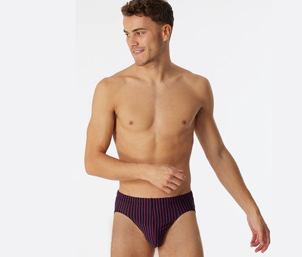 Homme torse nu portant un slip Supermini SCHIESSER à rayures rouges, regardant à droite et souriant.