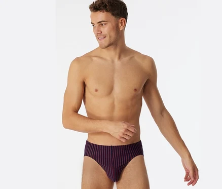 Homme torse nu portant un slip Supermini SCHIESSER à rayures rouges, regardant à droite et souriant.