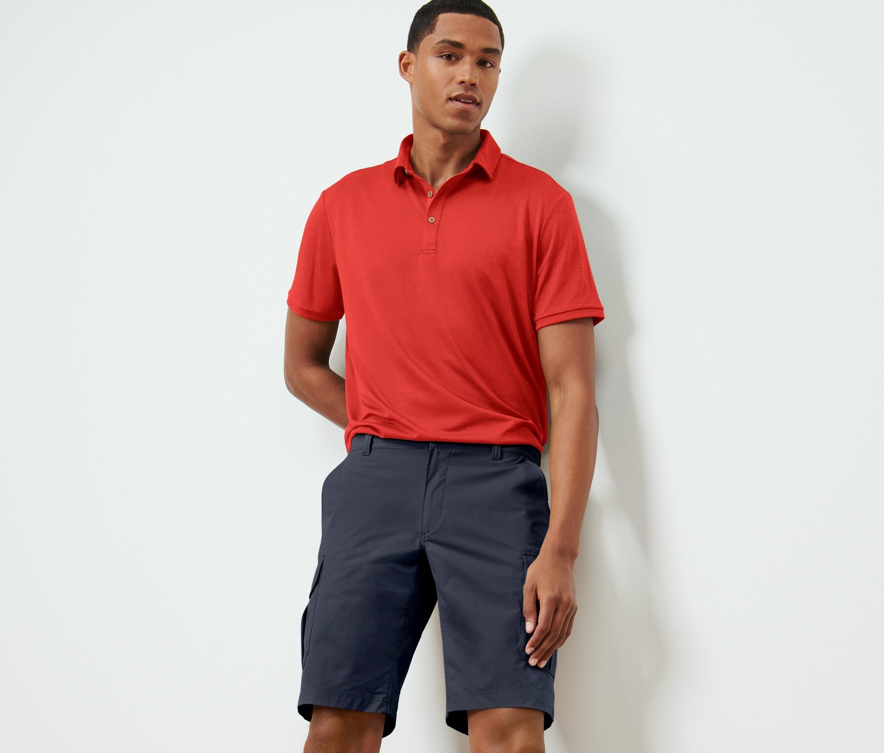 Un homme pose en polo rouge et short technique bleu.