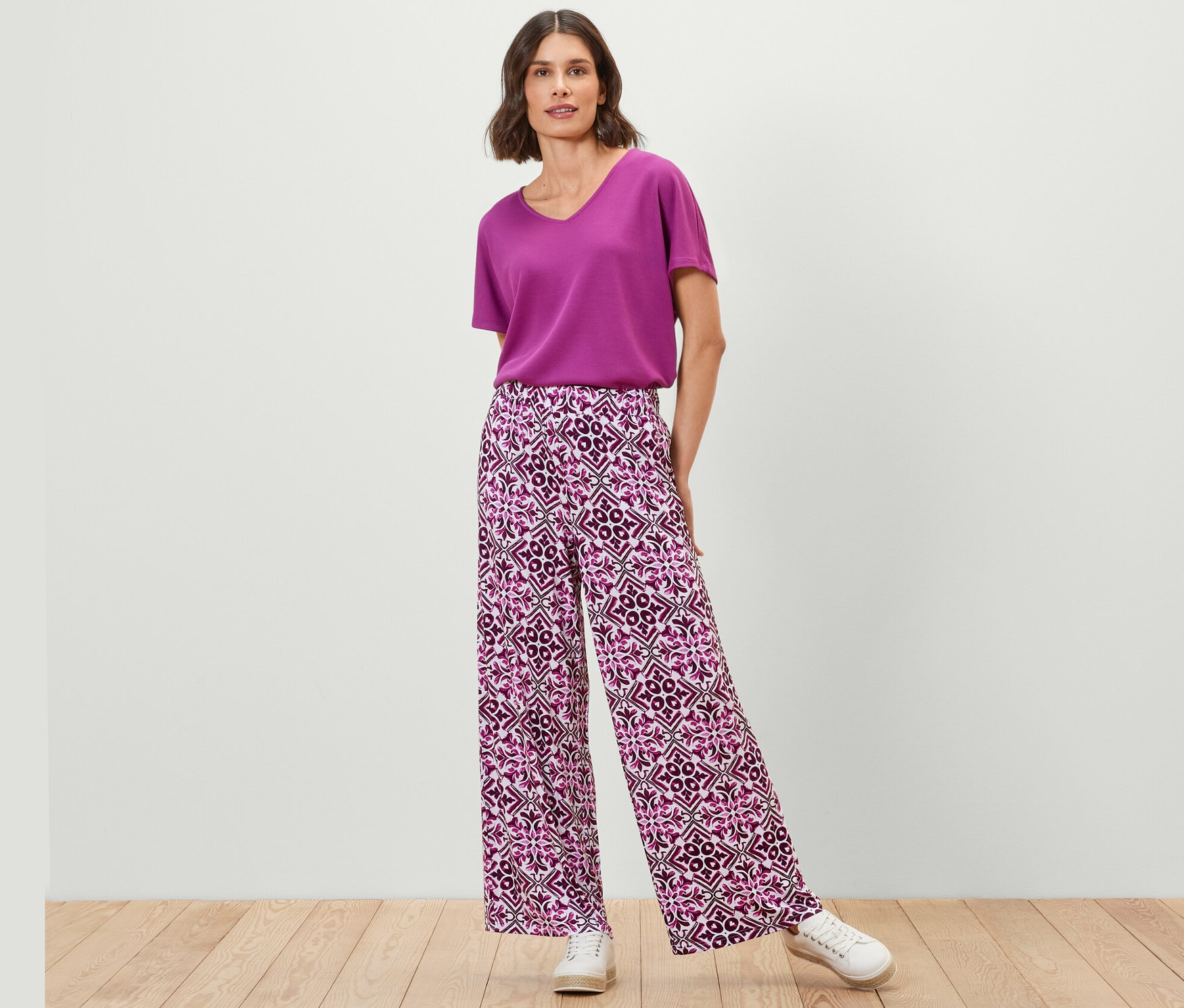 Femme posant en pantalon palazzo imprimé, baies et haut violet.