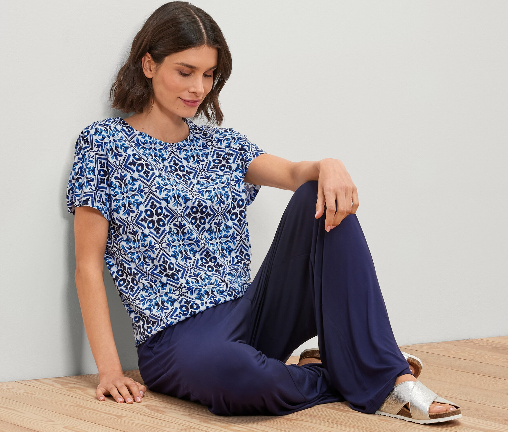 Femme assise par terre portant une blouse imprimée bleue.