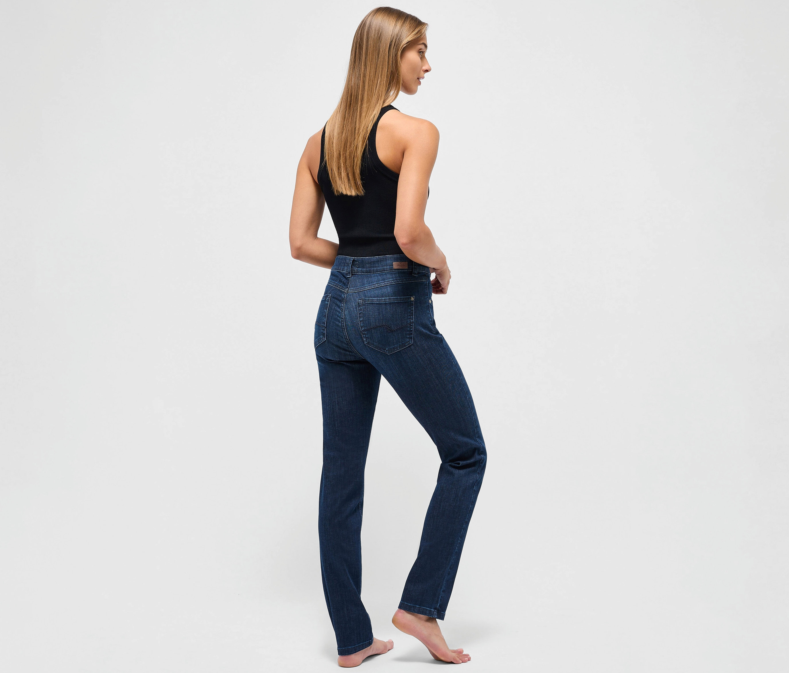 Une femme se tient dos à la caméra et porte un jean Angels « Cici » coupe étroite bleu foncé et un débardeur noir.