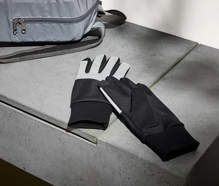 Un sac à dos gris et une paire de gants noirs sont posés sur un banc en béton.