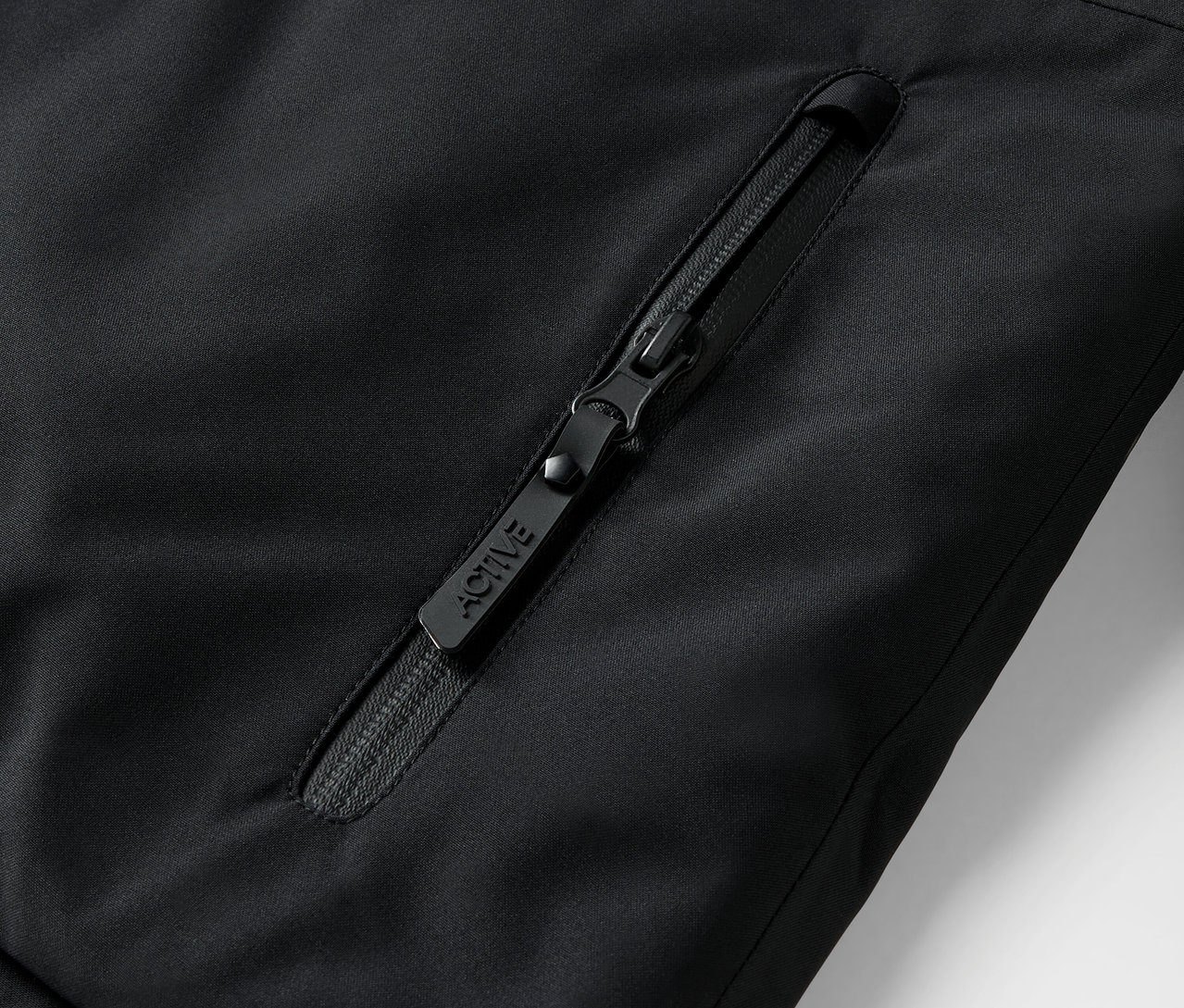 Gros plan d'une fermeture éclair noire sur une veste avec l'inscription ACTIVE.