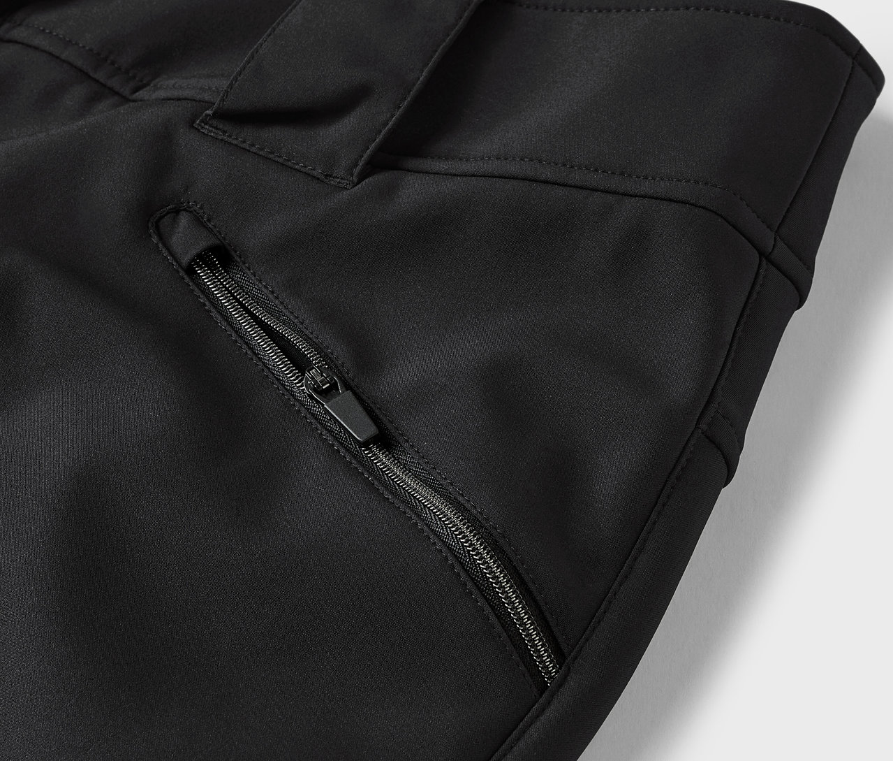 Détail d'un pantalon noir avec une poche zippée.