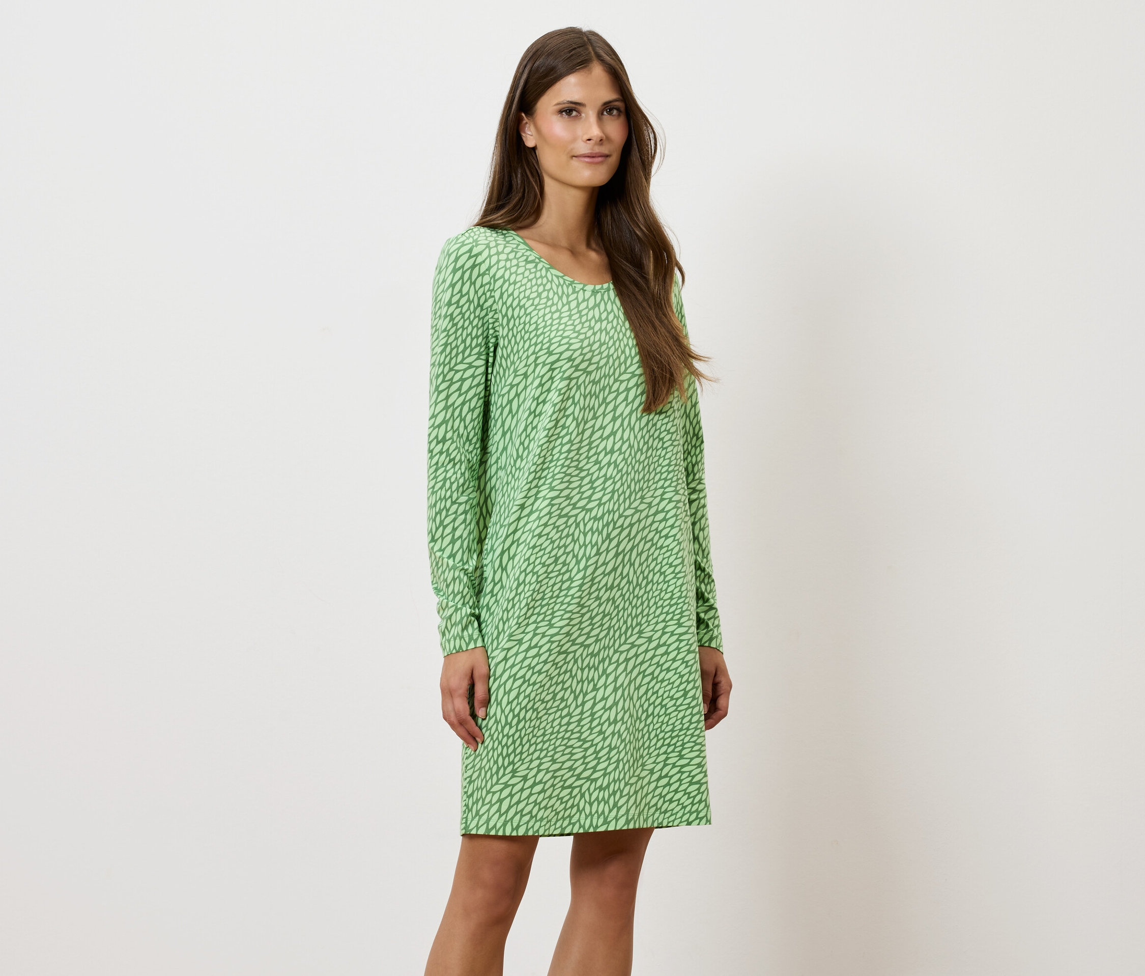 Une femme debout pose dans une robe verte à motifs à manches longues.