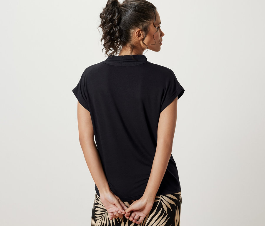 Une femme vue de dos porte une blouse noire à encolure en V et un pantalon à motif de feuilles.
